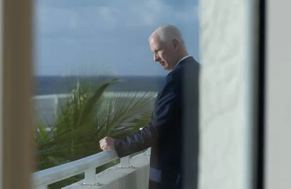 A man looks out at the ocean from a balcony.