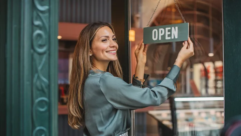 Women presenting an open sign at a shop.